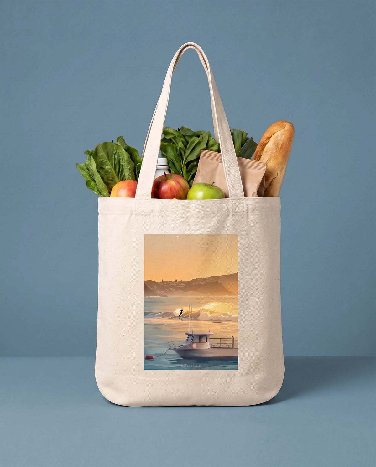 Coast & Compass Dawn Patrol tote bag packed with fresh groceries against a teal studio backdrop, cream cotton canvas printed with the Dawn Patrol artwork