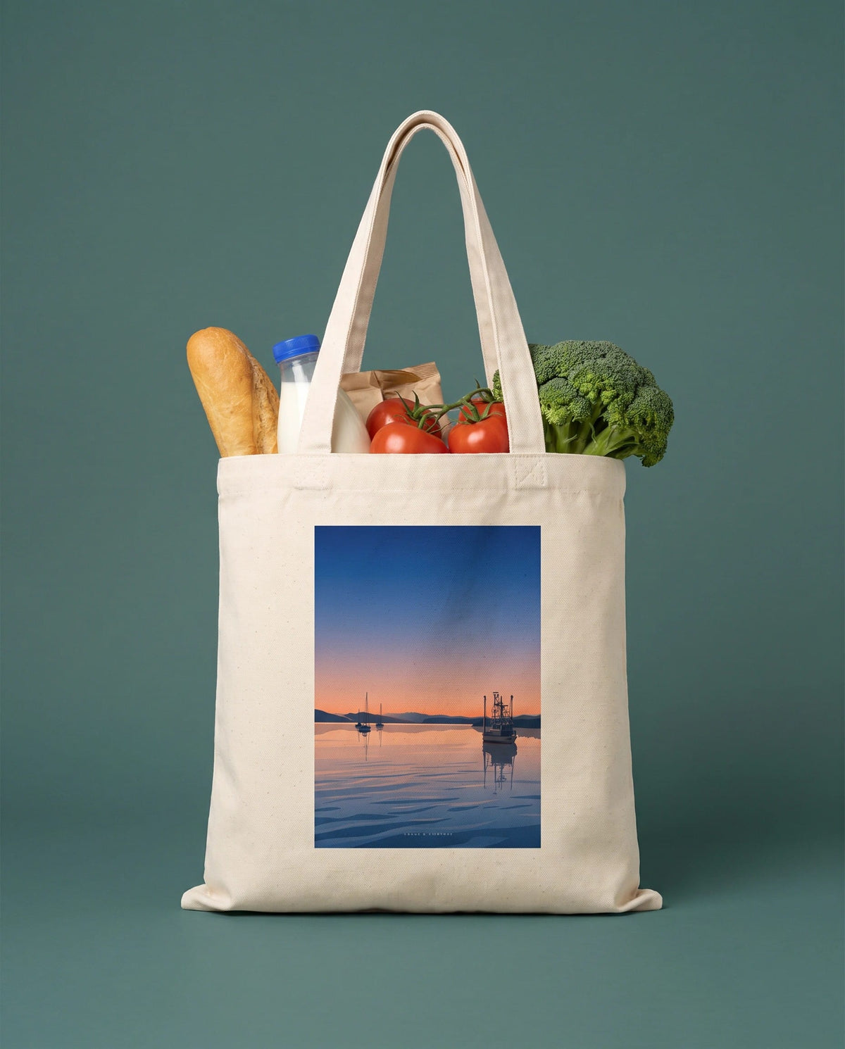 Coast & Compass Still Waters tote bag packed with fresh groceries against a teal studio backdrop, cream cotton canvas printed with the Still Waters artwork