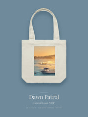 Dawn Patrol artwork printed on a cream cotton canvas tote bag — a surfer on a golden wave with a moored boat in the foreground