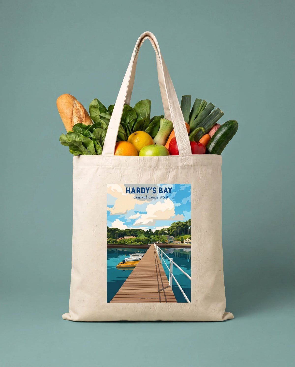 Coast & Compass Hardy's Bay tote bag packed with fresh groceries against a sage studio backdrop, cream cotton canvas printed with the Hardy's Bay Central Coast NSW poster design