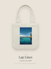 Lap Lines artwork printed on a cream cotton canvas tote bag — swimmers cutting laps in a tidal ocean pool with a figure at the rail