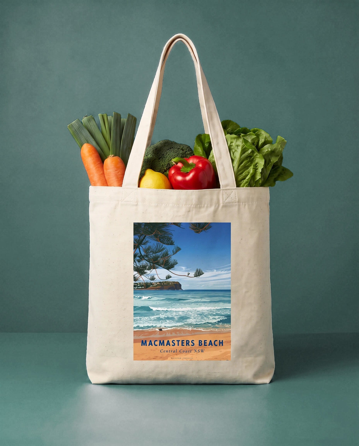 Coast & Compass Macmasters Beach tote bag packed with fresh vegetables against a teal studio backdrop, cream cotton canvas printed with the Macmasters Beach Central Coast NSW poster design