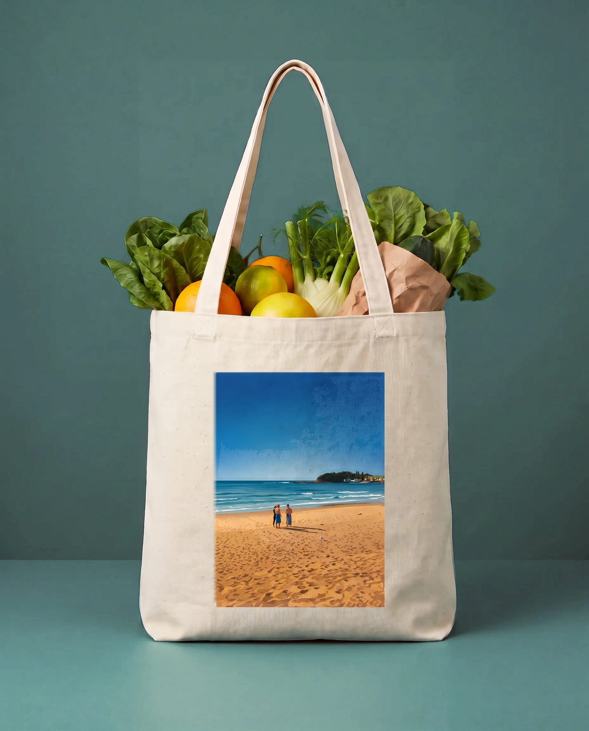 Coast & Compass Shoreline Gathering tote bag packed with fresh groceries against a teal studio backdrop, cream cotton canvas printed with the Shoreline Gathering artwork
