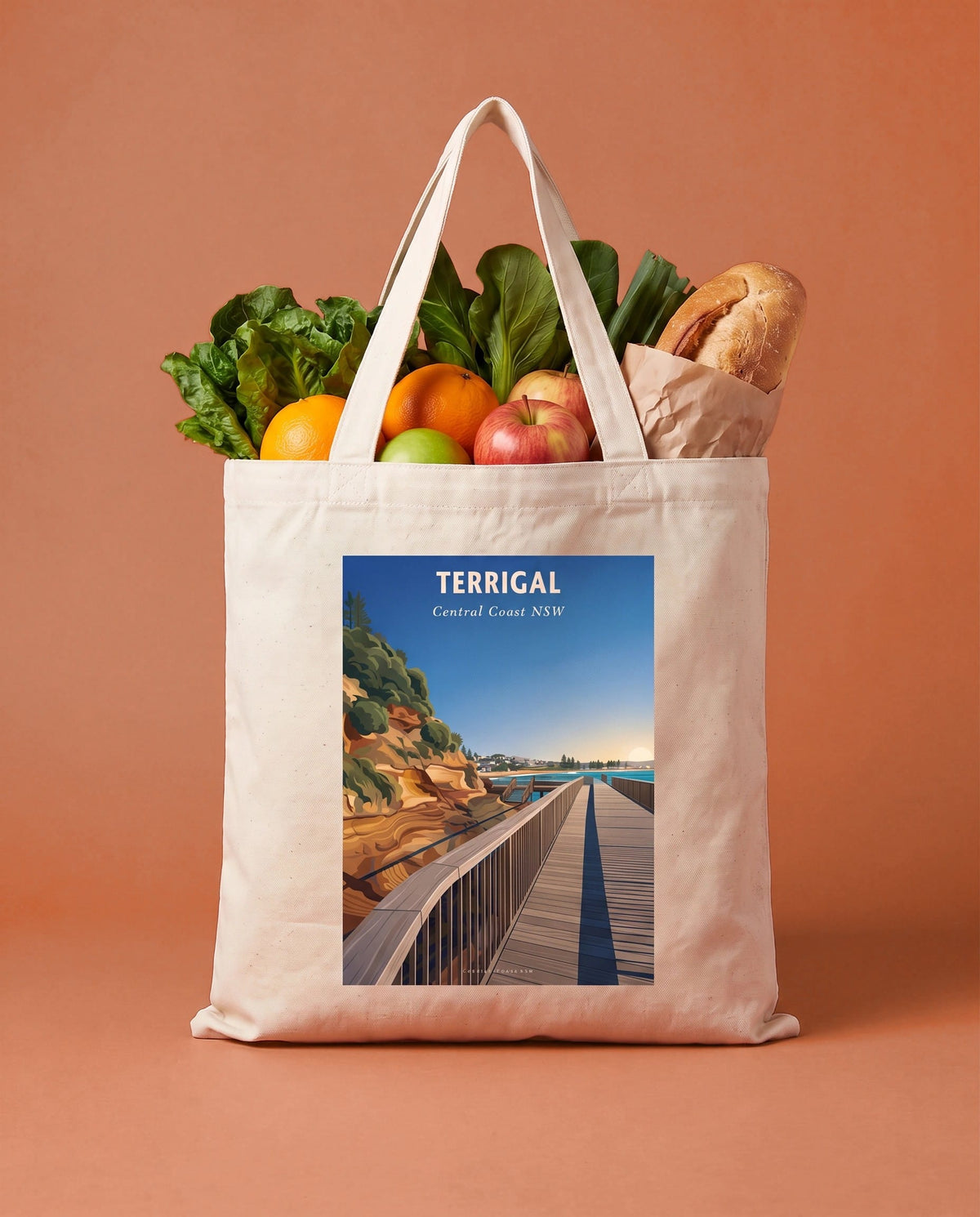Coast & Compass Terrigal Boardwalk tote bag packed with fresh groceries against a terracotta studio backdrop, cream cotton canvas printed with the Terrigal Boardwalk Central Coast NSW poster design