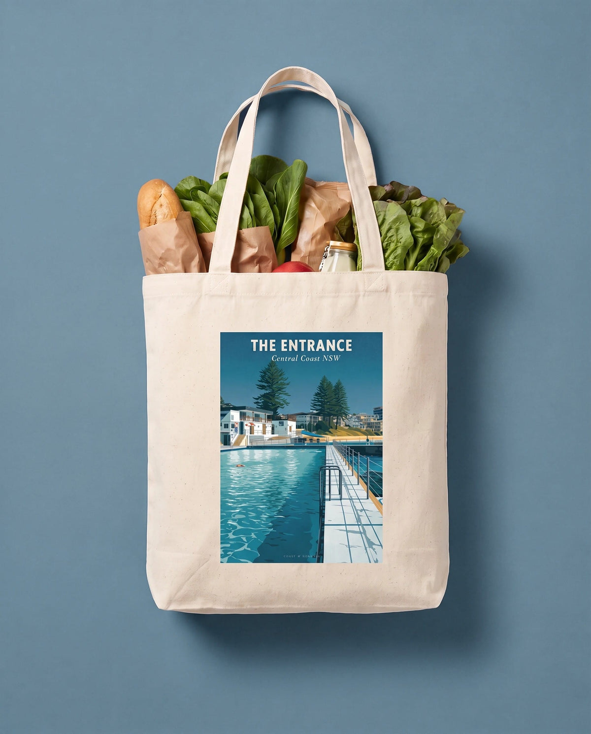 Coast & Compass The Entrance tote bag packed with fresh groceries against a slate blue studio backdrop, cream cotton canvas printed with The Entrance Central Coast NSW poster design